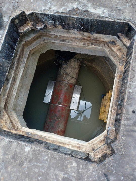 Vue plongeante dans une trappe technique montrant une canalisation prête à recevoir un débitmètre clamp-on sans perçage.