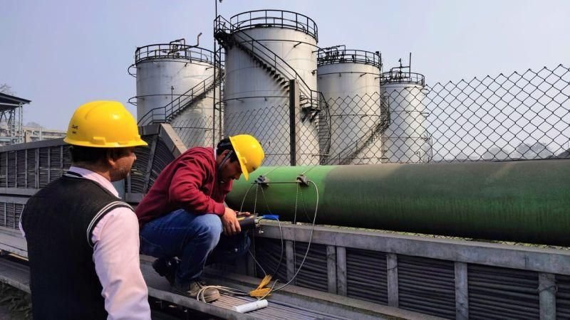Opérateur équipé d’un casque installant un débitmètre clamp-on non intrusif sur une conduite industrielle verte.